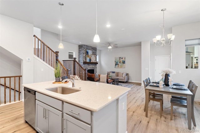 kitchen with pendant lighting, dishwasher, an island with sink, sink, and a brick fireplace