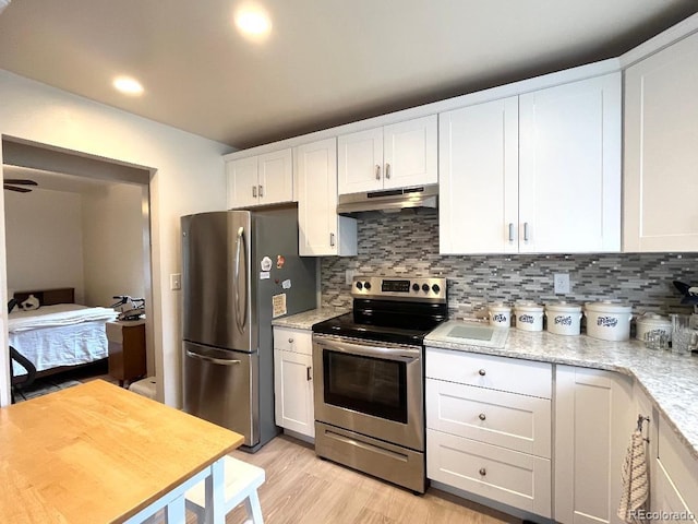 2285 S Knox Ct, Denver, CO 80219 - kitchen with appliances with stainless steel finishes, under cabinet range hood, white cabinetry, decorative backsplash, and light wood-style flooring