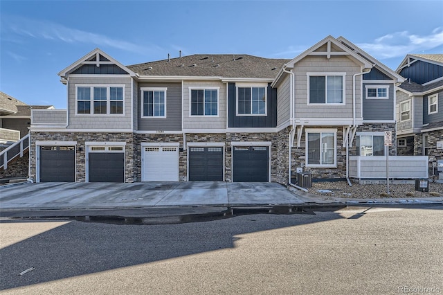 multi unit property with driveway, stone siding, a garage, and central AC