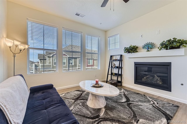 living area with baseboards, visible vents, a glass covered fireplace, ceiling fan, and wood finished floors