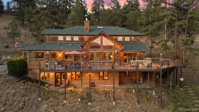 rear view of house featuring a shingled roof, a chimney, and a deck