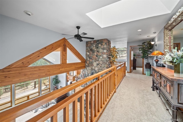 corridor featuring an upstairs landing, vaulted ceiling with skylight, and light carpet