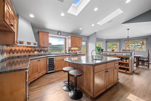 kitchen with a sink, a kitchen island with sink, light wood-style flooring, and beverage cooler