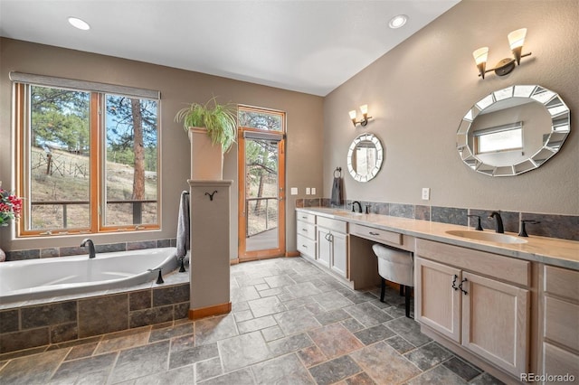 full bath featuring double vanity, a sink, stone tile floors, and a healthy amount of sunlight