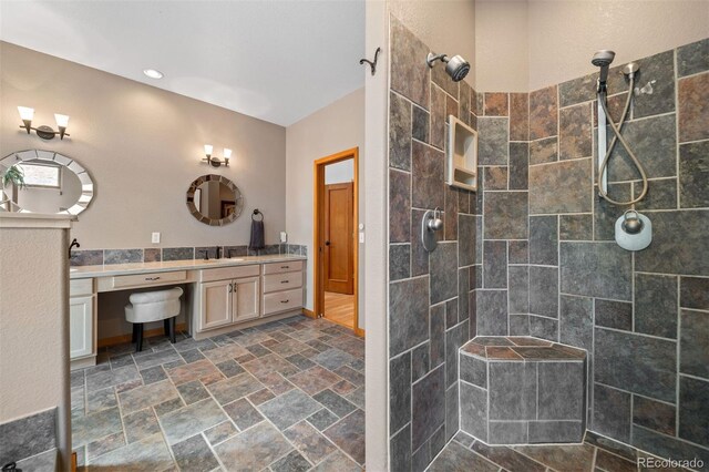 bathroom with stone tile flooring, vanity, and tiled shower