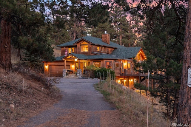 rustic home with roof with shingles, a chimney, an attached garage, and driveway