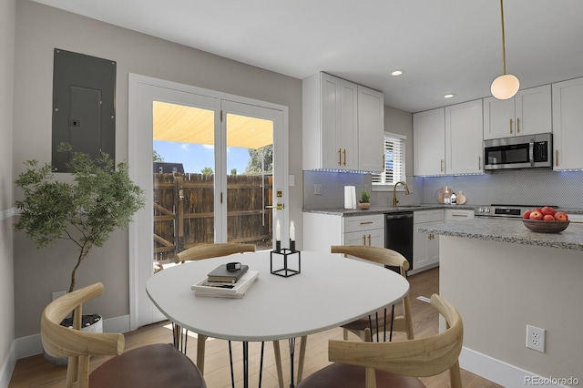 kitchen with electric panel, hanging light fixtures, appliances with stainless steel finishes, tasteful backsplash, and white cabinetry