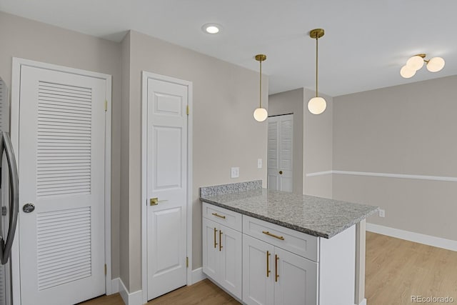 kitchen featuring kitchen peninsula, white cabinets, hanging light fixtures, and light hardwood / wood-style floors