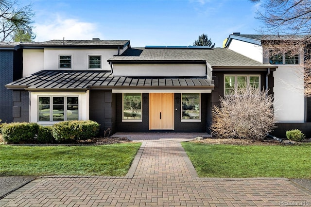 view of front of property with brick siding, a chimney, metal roof, a standing seam roof, and a front yard