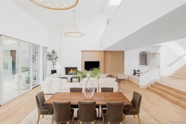 dining area featuring light wood-style floors, a notable chandelier, a towering ceiling, and stairs