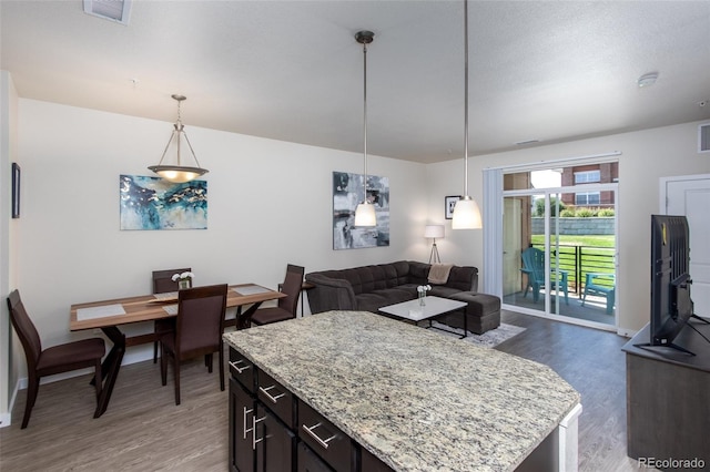 kitchen with a center island, dark hardwood / wood-style floors, light stone counters, and hanging light fixtures