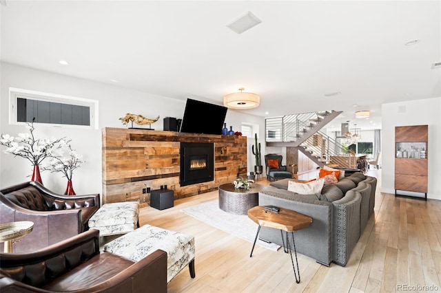 living area featuring recessed lighting, a glass covered fireplace, light wood-style floors, and stairs