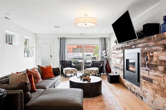living room with a glass covered fireplace, light wood-style floors, and visible vents