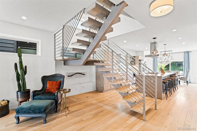 stairs with wood finished floors, recessed lighting, and a chandelier