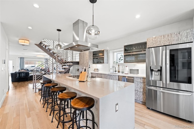 kitchen with island exhaust hood, a kitchen bar, stainless steel appliances, and light wood-type flooring