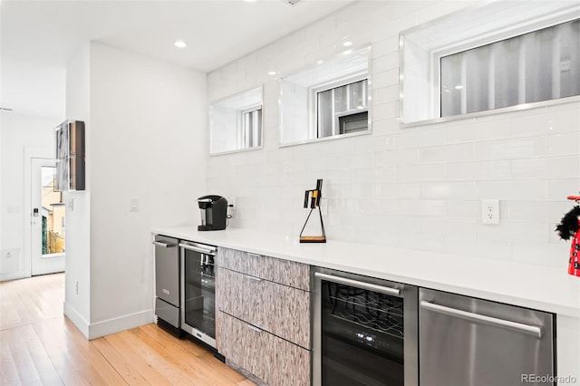 bar with light wood-type flooring, wine cooler, stainless steel dishwasher, and tasteful backsplash