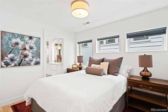 bedroom featuring connected bathroom, baseboards, wood finished floors, and visible vents