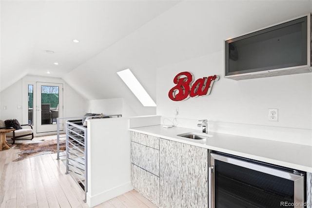 interior space with beverage cooler, a sink, light wood-style floors, vaulted ceiling with skylight, and bar