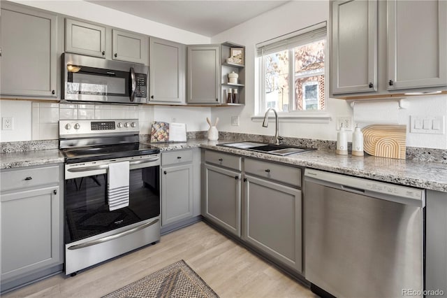 kitchen with appliances with stainless steel finishes, gray cabinetry, light wood-type flooring, backsplash, and sink