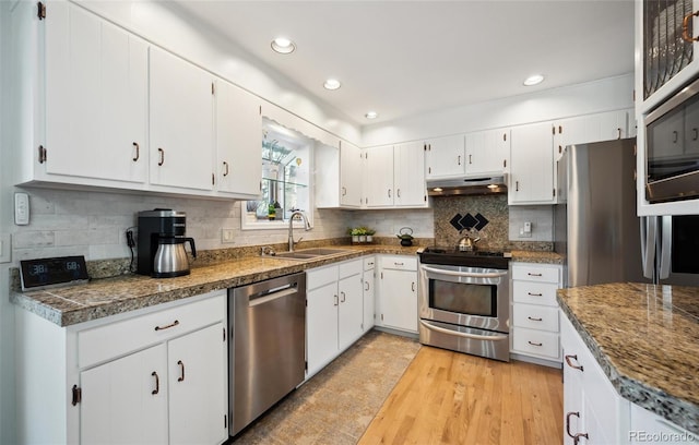 kitchen with appliances with stainless steel finishes, tasteful backsplash, light wood-type flooring, white cabinets, and sink