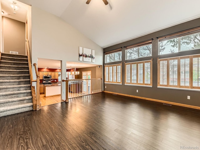 unfurnished living room with dark wood finished floors, a chandelier, ceiling fan, baseboards, and high vaulted ceiling