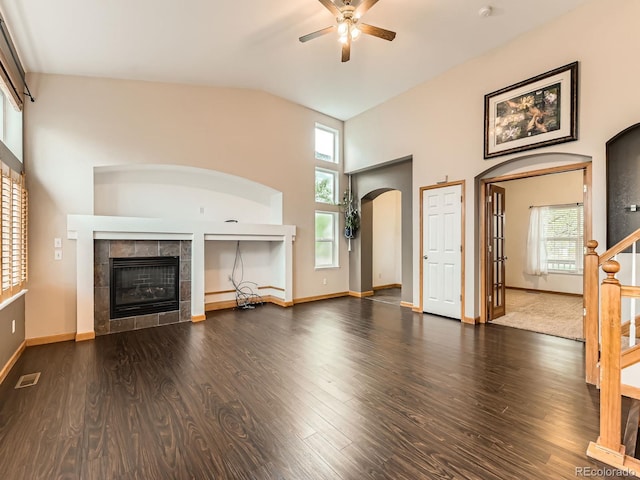 unfurnished living room with arched walkways, a ceiling fan, a tile fireplace, wood finished floors, and a towering ceiling