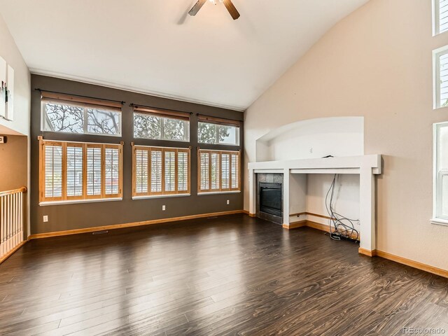 unfurnished living room featuring healthy amount of natural light, a ceiling fan, a fireplace, dark wood finished floors, and high vaulted ceiling