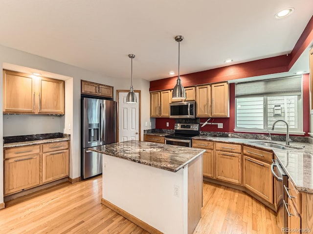 kitchen featuring appliances with stainless steel finishes, a sink, dark stone countertops, a kitchen island, and light wood-style floors
