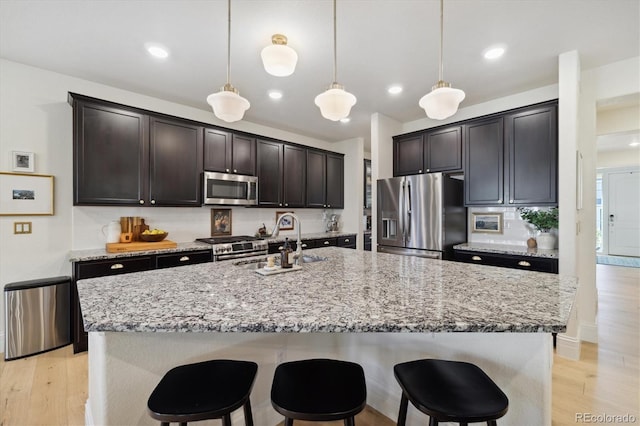 kitchen featuring appliances with stainless steel finishes, a sink, light stone counters, a breakfast bar, and an island with sink