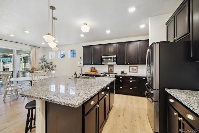 kitchen featuring a kitchen breakfast bar, an island with sink, recessed lighting, light wood-style flooring, and stainless steel appliances