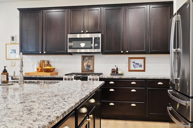 kitchen featuring a sink, decorative backsplash, appliances with stainless steel finishes, and light stone countertops