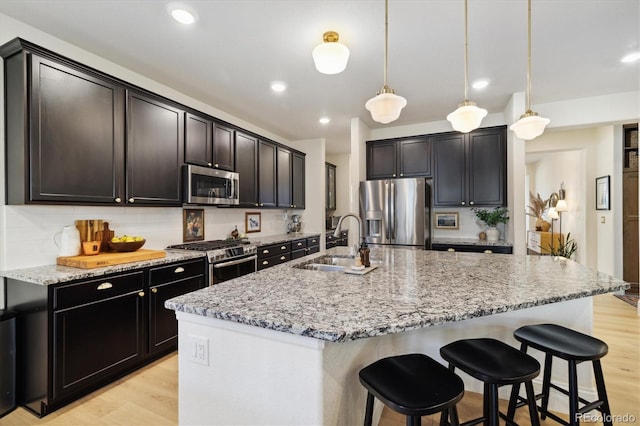 kitchen featuring appliances with stainless steel finishes, light stone counters, a sink, light wood-style flooring, and decorative backsplash