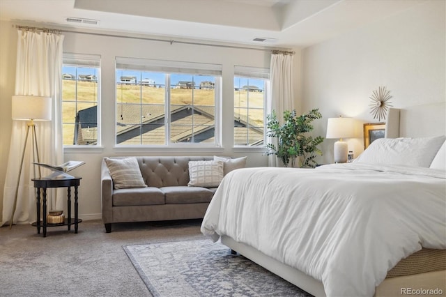 carpeted bedroom featuring baseboards, visible vents, and a raised ceiling