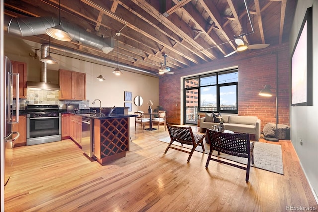 kitchen with a peninsula, appliances with stainless steel finishes, dark countertops, wall chimney range hood, and open floor plan