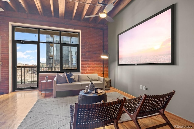 living area featuring ceiling fan, beam ceiling, wood finished floors, and brick wall