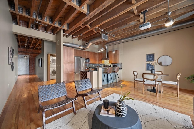 living room featuring a high ceiling, stacked washer and clothes dryer, and light wood-type flooring