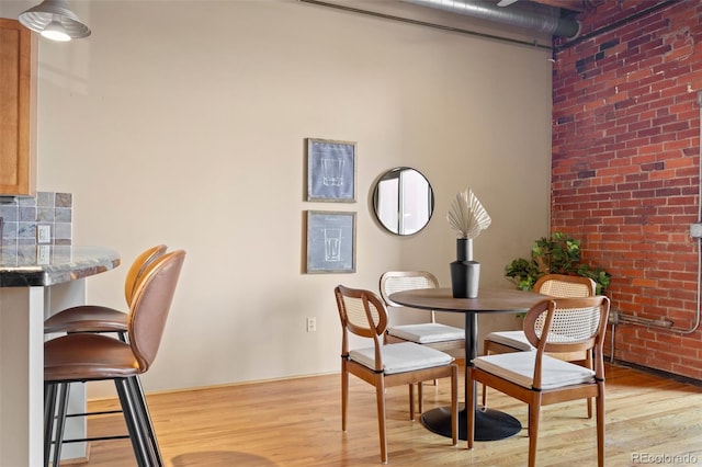 dining space featuring light wood-style floors and brick wall