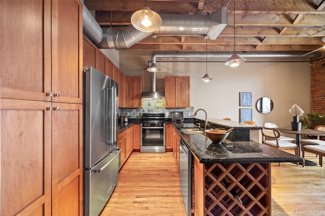 kitchen with light wood-type flooring, a sink, a peninsula, appliances with stainless steel finishes, and wall chimney exhaust hood