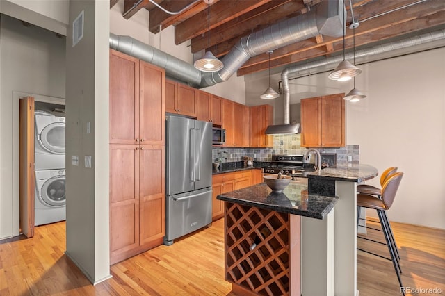 kitchen with a breakfast bar area, visible vents, stacked washing maching and dryer, a towering ceiling, and appliances with stainless steel finishes