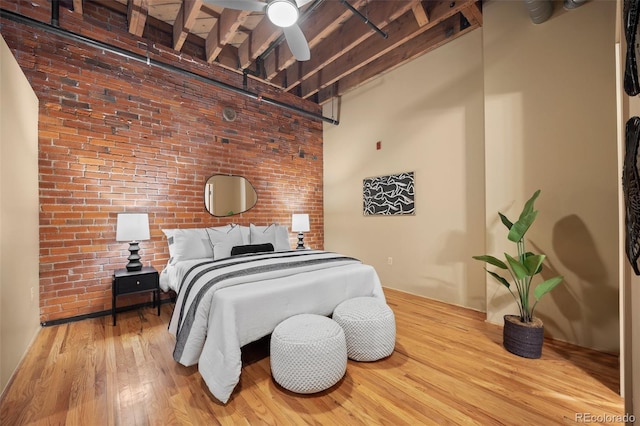 bedroom with brick wall, a high ceiling, and wood finished floors