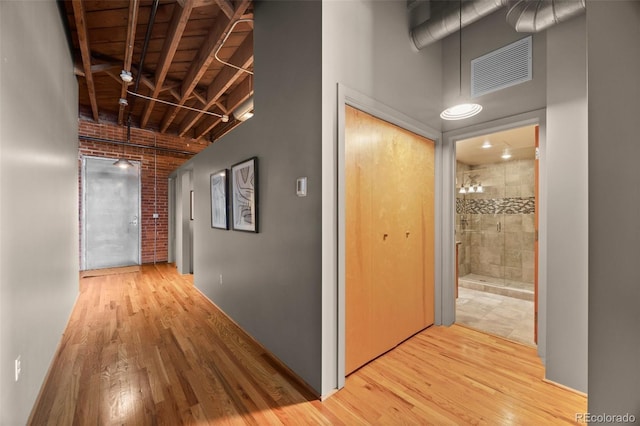 hallway with light wood finished floors, visible vents, brick wall, and a towering ceiling