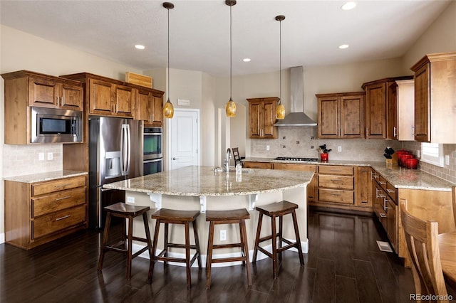 kitchen with a sink, brown cabinets, appliances with stainless steel finishes, and wall chimney range hood