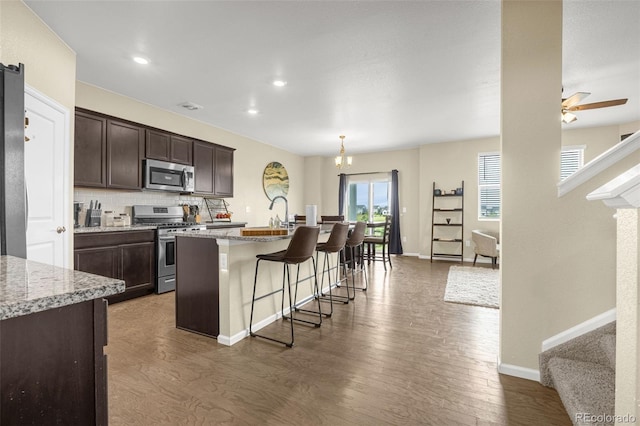 91 S Quantock St, Aurora, CO 80018 - kitchen with stainless steel appliances, dark wood-type flooring, dark brown cabinets, a breakfast bar, and recessed lighting