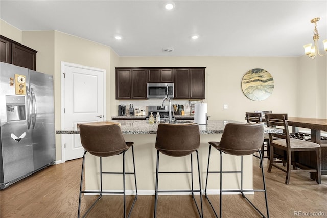 91 S Quantock St, Aurora, CO 80018 - kitchen with appliances with stainless steel finishes, wood finished floors, dark brown cabinetry, light stone counters, and recessed lighting