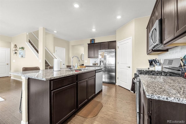91 S Quantock St, Aurora, CO 80018 - kitchen featuring stainless steel appliances, wood finished floors, dark brown cabinets, a breakfast bar area, and a kitchen island with sink