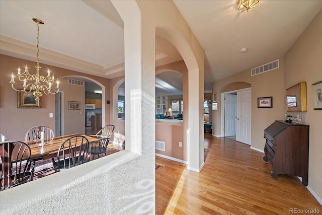 dining space with arched walkways, visible vents, and light wood finished floors