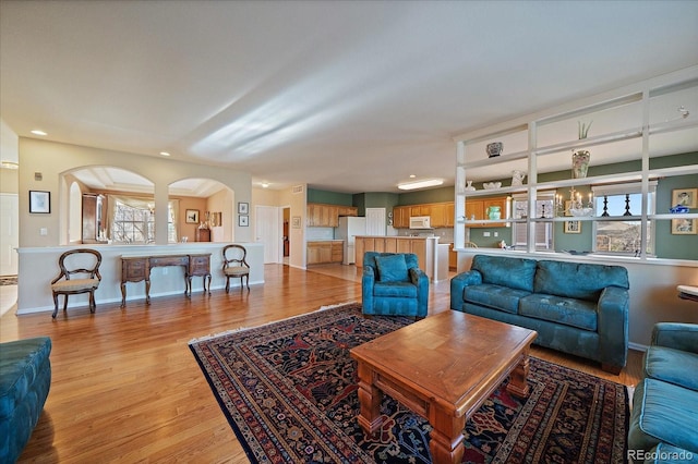 living area featuring arched walkways, recessed lighting, light wood-style flooring, and baseboards