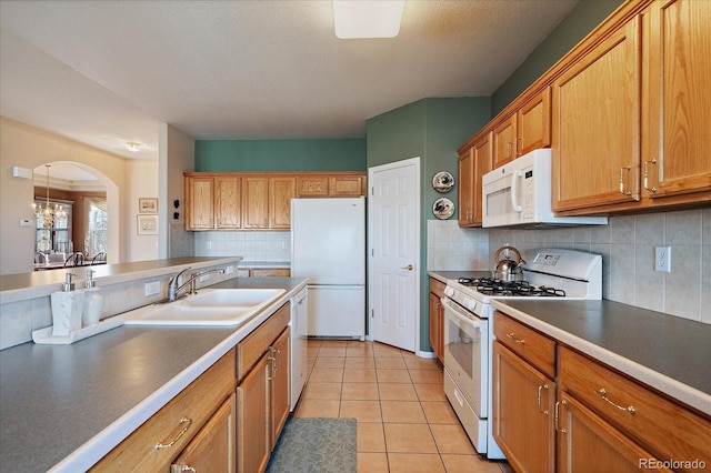 kitchen featuring white appliances, light tile patterned flooring, arched walkways, a sink, and backsplash