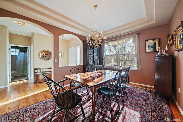 dining space featuring a tray ceiling, baseboards, a notable chandelier, and wood finished floors