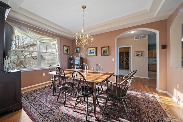 dining space with a raised ceiling, wood finished floors, visible vents, and baseboards